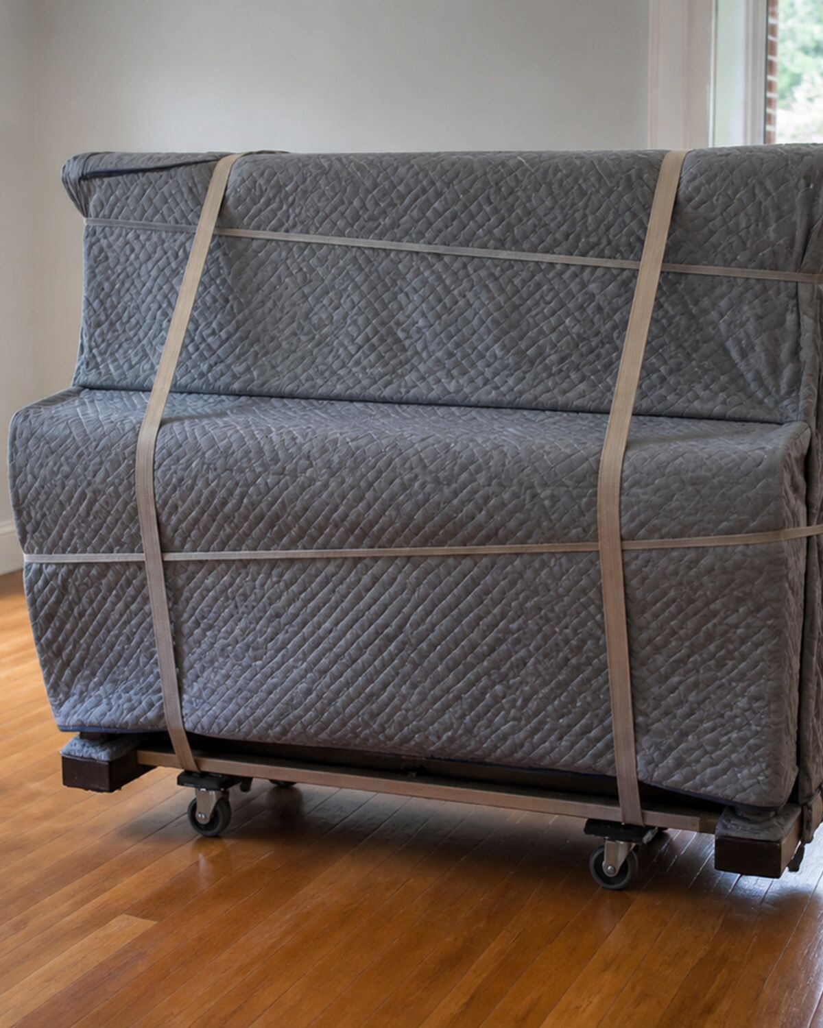 An upright piano wrapped in moving blankets and strapped to a piano dolly
